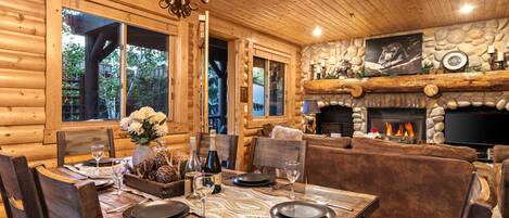 A cozy log cabin interior with a dining area, fireplace, and stone wall decor.