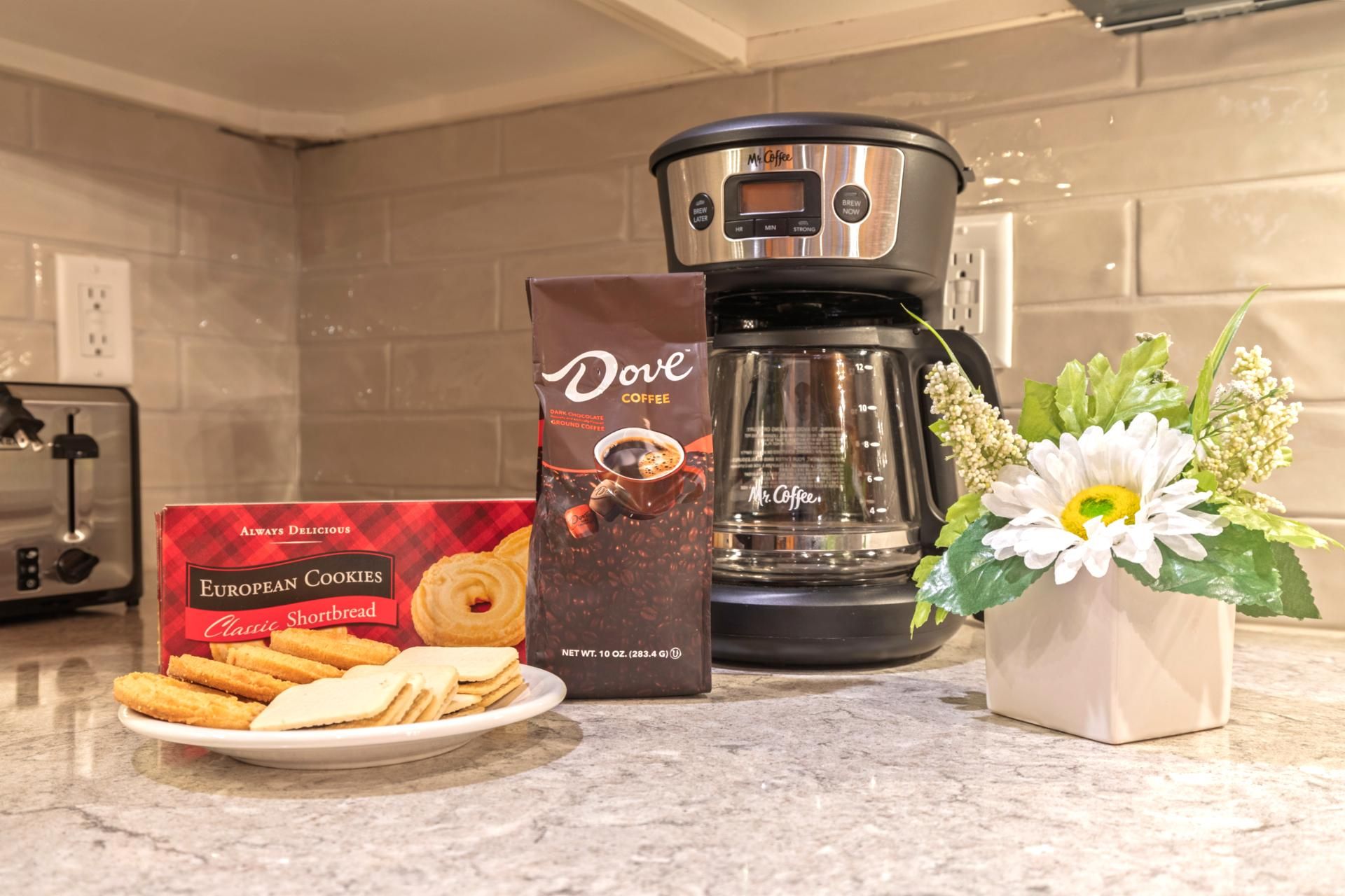Un comptoir de cuisine avec une machine à café, une boîte de biscuits européens et une assiette de biscuits.