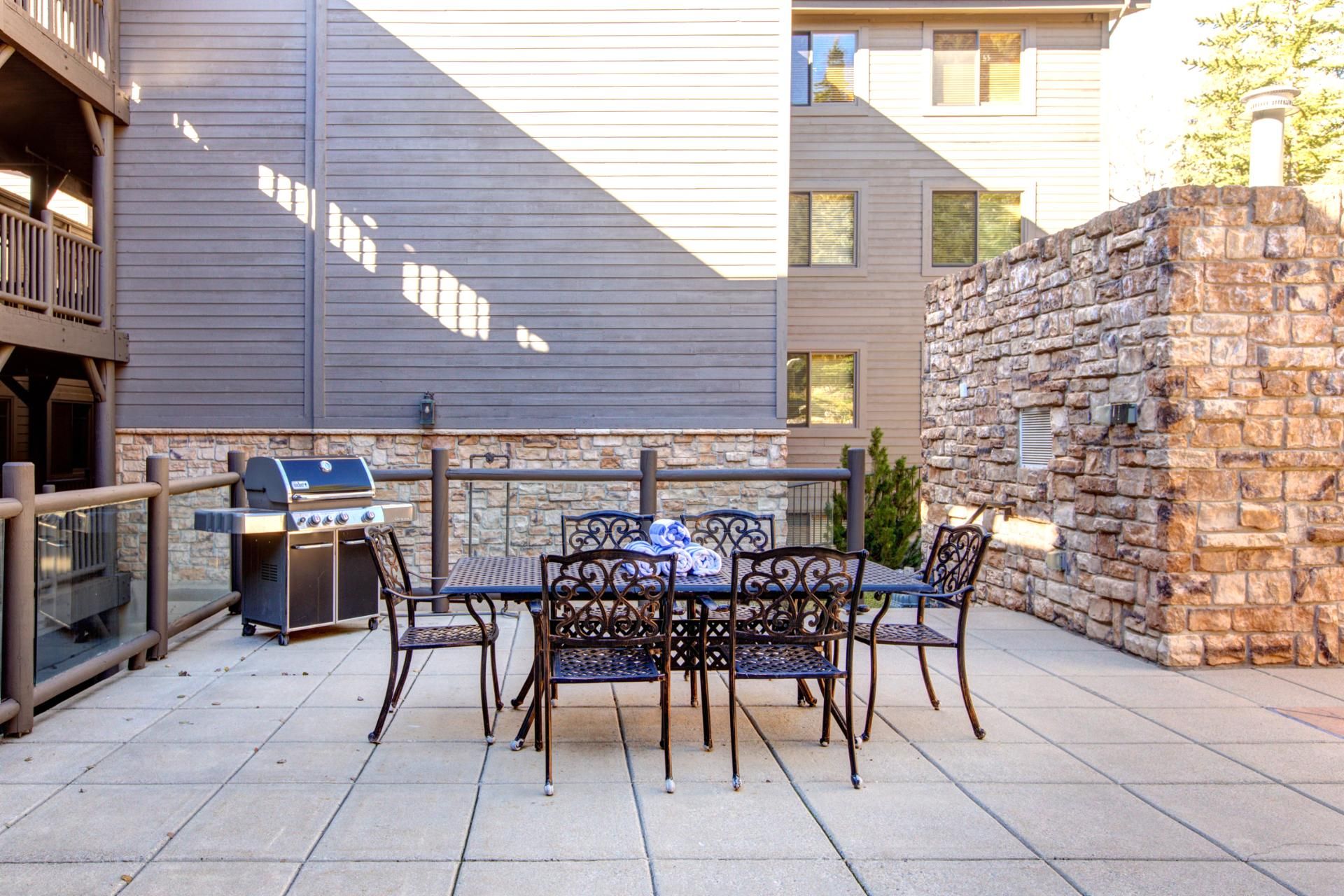 An outdoor patio with a grill, table, and chairs.