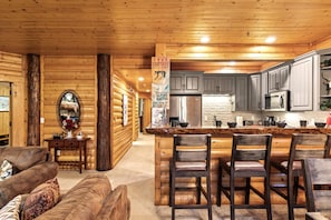 Interior de una cabaña de madera con cocina, comedor y barra.