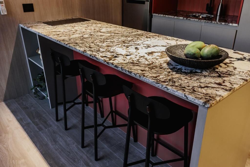 Una cocina con encimera de granito, un bol de fruta y taburetes negros.