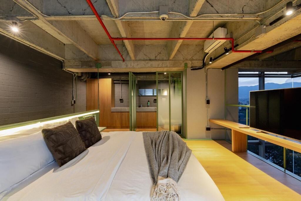 A modern hotel room with a large bed, a bench, a TV, and a view of the mountains.