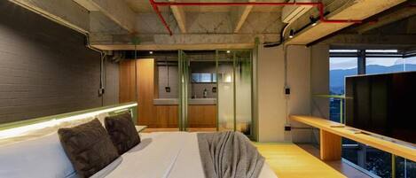 A modern hotel room with a large bed, a bench, a TV, and a view of the mountains.