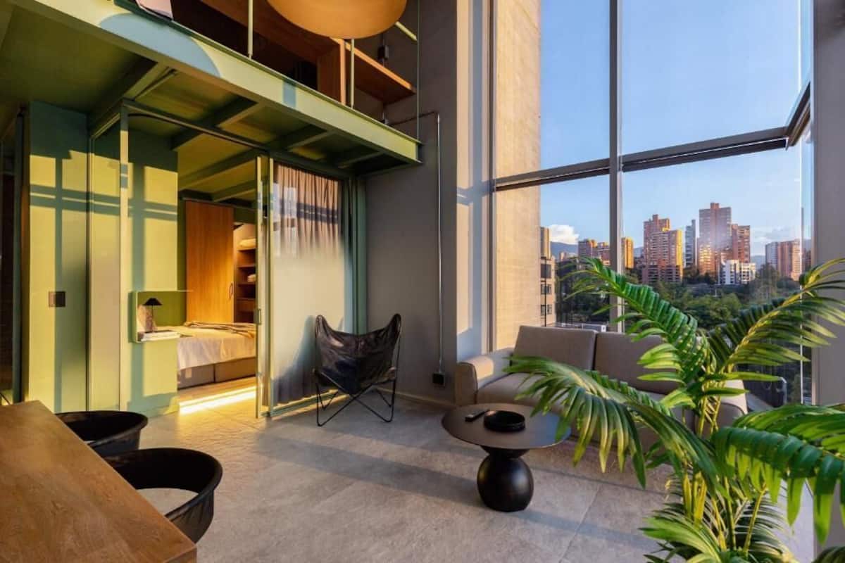 Ein modernes Interieur mit Bett, Sitzgelegenheit und großen Fenstern mit Blick auf die Stadt.