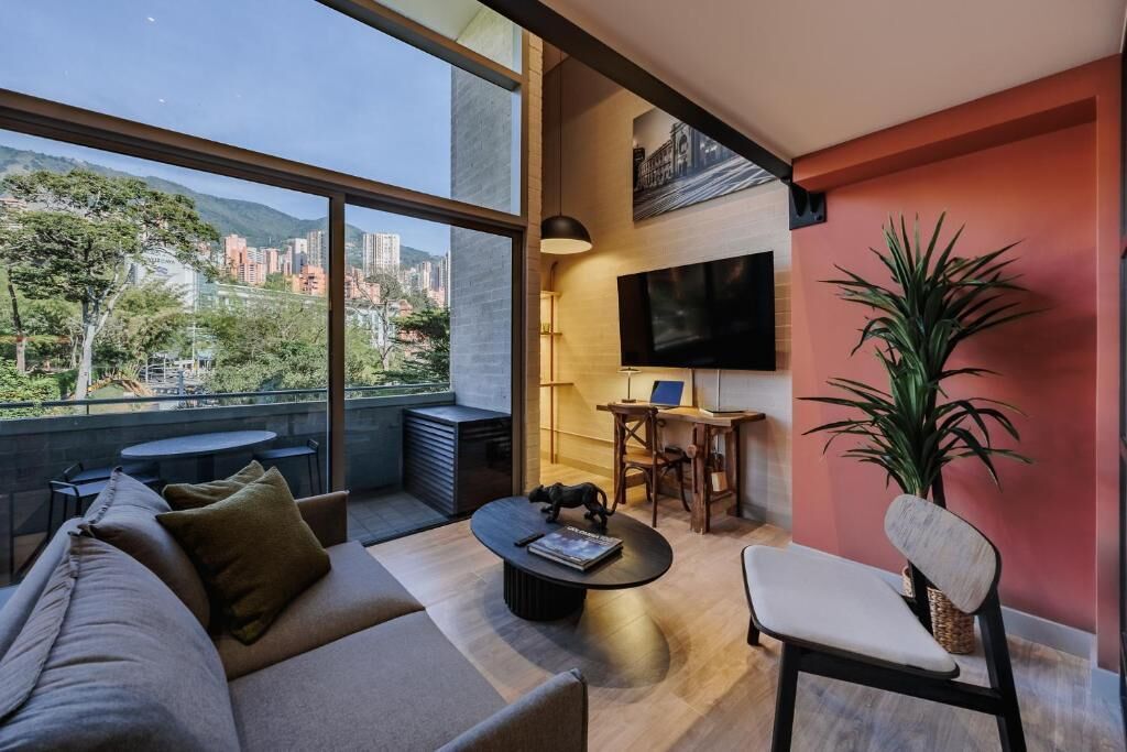 Een moderne woonkamer met een bank, salontafel en stoel, een aan de muur bevestigde televisie, en een groot raam met uitzicht op de stad.