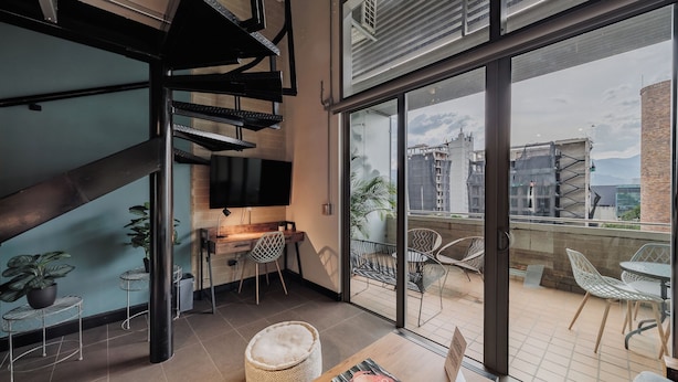A modern living room with a large TV, a wooden desk, and a comfortable seating area with chairs. - H10 Provenza (Medellín)