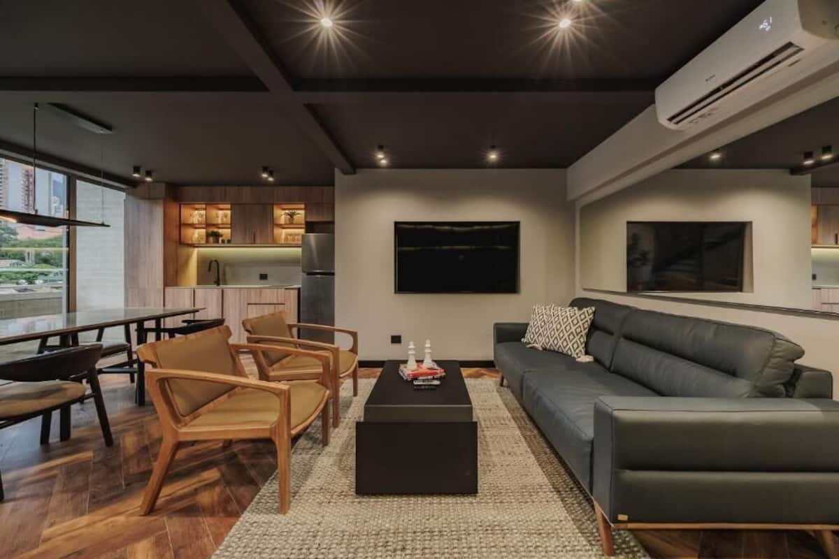 Ein modernes Wohnzimmer mit einer Couch, Sesseln, einem Couchtisch und einem Fernseher.