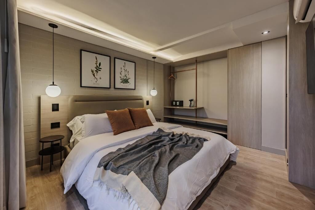 A modern bedroom with a large bed, two bedside tables, a small side table, a wardrobe, and a hanging light fixture.