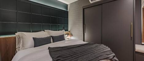 A modern bedroom with a large bed, a dark headboard, and a wardrobe.