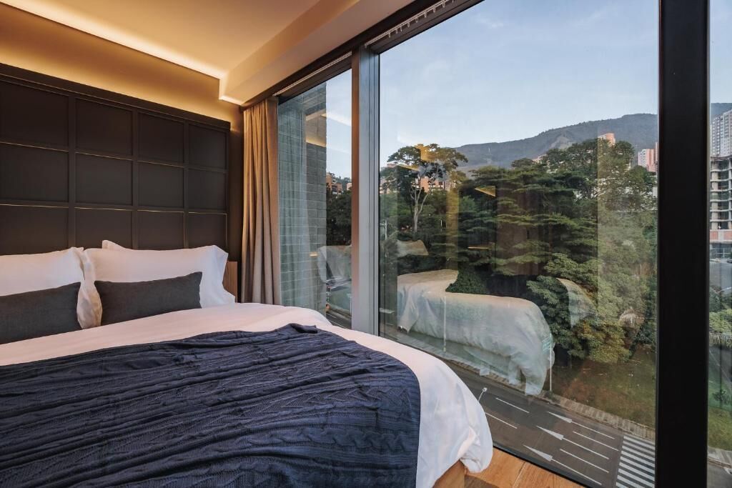 Een moderne hotelkamer met een groot bed, een glazen wand en uitzicht op een bergachtig landschap.