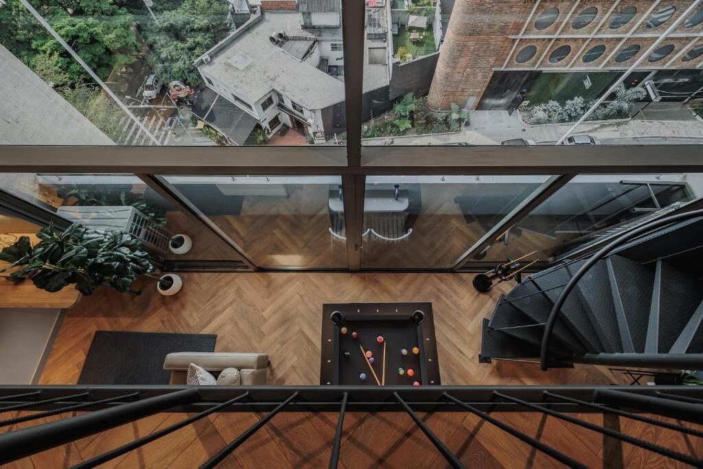 Una habitación espaciosa con techos altos, una mesa de billar, un sofá y una escalera.