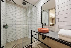 A modern bathroom with white tiled walls, a glass shower enclosure, and a black countertop with a round orange sink. - H10 Provenza (Medellín)