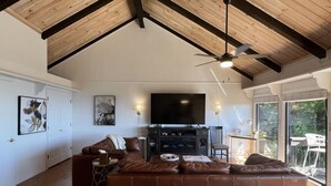 A spacious living room with a large brown leather sofa, a flat-screen TV, and a ceiling fan.