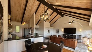 A spacious kitchen with a dining area, wooden ceiling beams, and a modern chandelier.