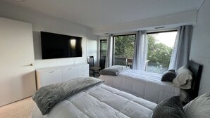 A bedroom with two beds, a TV mounted on the wall, and a window with curtains.