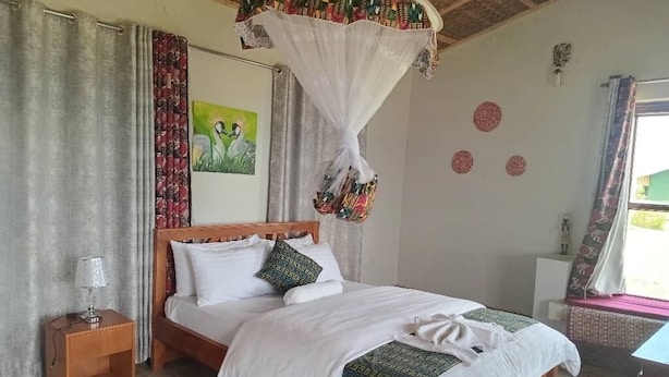 A bedroom with a bed, nightstand, and a window with curtains. - ngirisi hill silverback  lodge-bwindi (Bwindi)