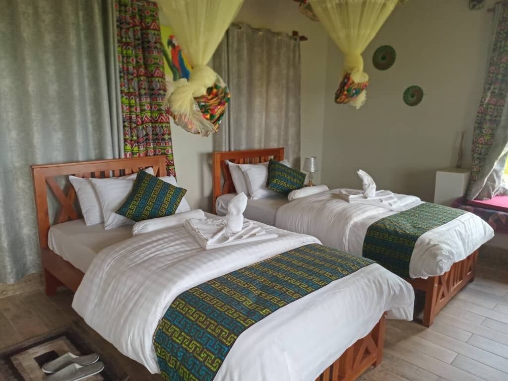 Habitación de hotel con dos camas de madera, cada una con ropa blanca y colchas estampadas en verde.