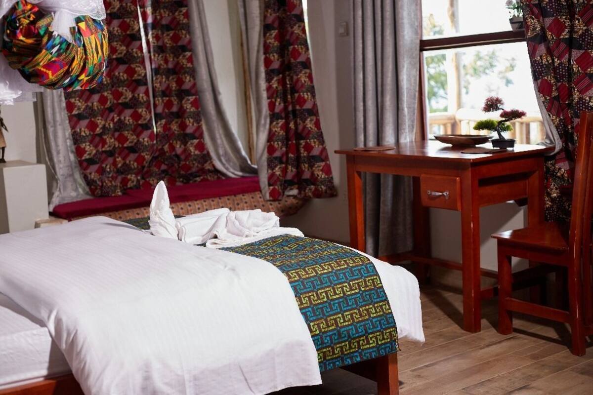 A neatly made bed with a patterned bedspread, a wooden desk with a small plant, and a chair.