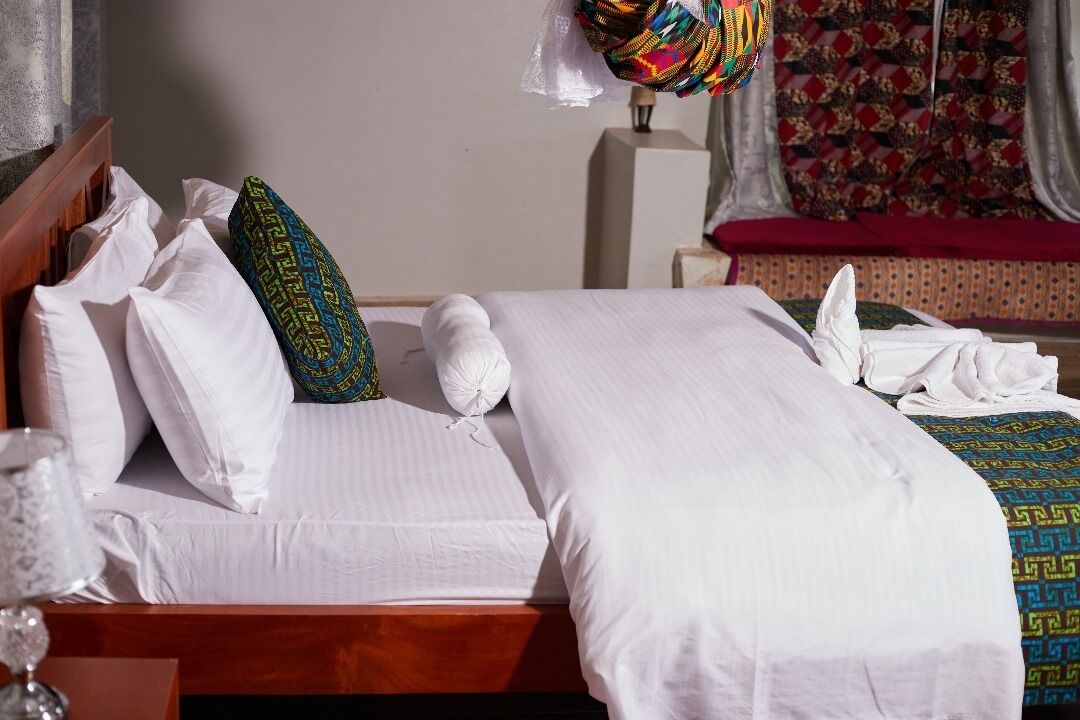 A neatly made bed with white linens and decorative pillows, a wooden headboard, and a bedside table with a glass.