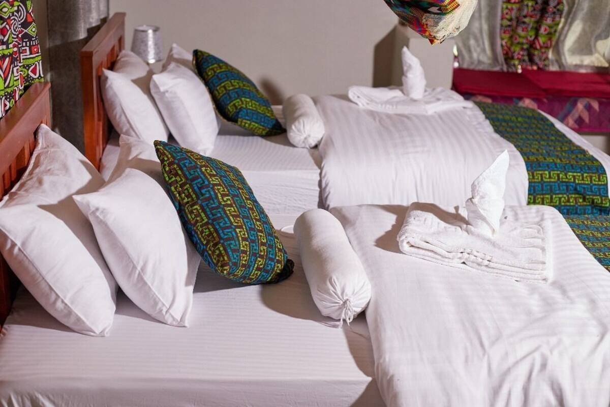 A neatly made bed with white linens and patterned pillows, a wooden headboard, and a small bedside table with a lamp.