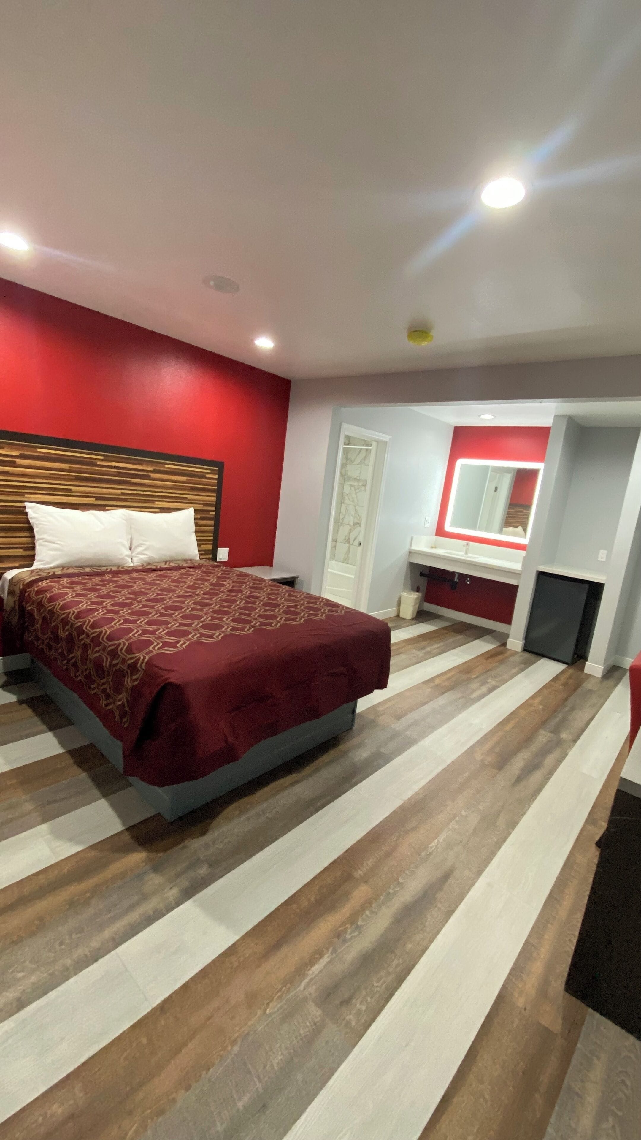 A hotel room with a bed, a vanity with a mirror, and a small kitchenette.