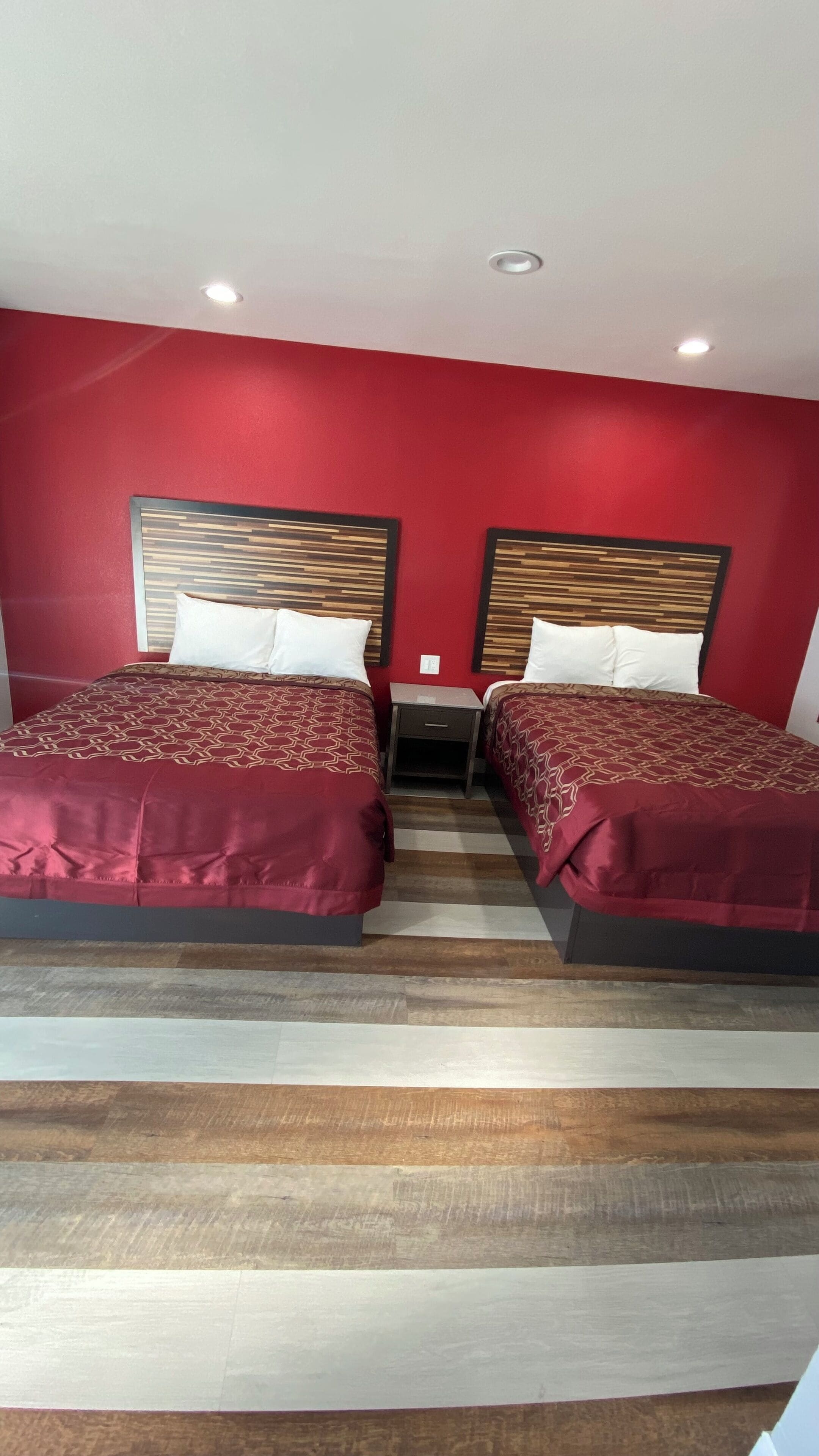 Habitación de hotel con dos camas, paredes rojas y piso de madera.