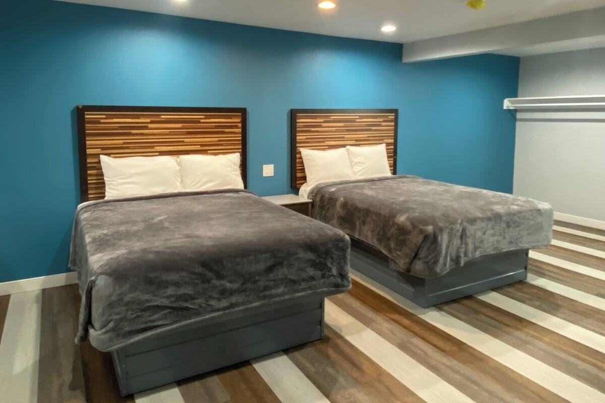 A room with two beds, blue walls, and a striped wooden floor.