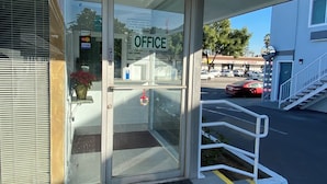 A building entrance with a glass door labeled "OFFICE," a small potted plant, and a doormat. - Plaza inn Motel - Los Angeles area (Rosemead)