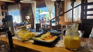 Ein Frühstücksbuffet mit verschiedenen Früchten und einem Saftkrug, mit Blick auf eine gebirgige Landschaft.