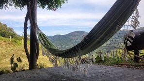 Un hamac est suspendu entre deux arbres, au-dessus d’une zone pavée, et offre une vue sur des collines verdoyantes à l’arrière-plan.