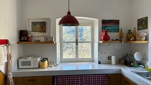 A kitchen with a window, white tiles, a microwave, a red pendant light, and various kitchen items on shelves. - Historical Villa 'The Birdhouse' - Garden & Views (Monterosso al Mare)