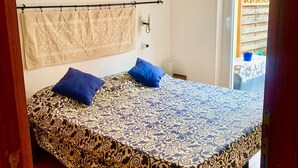 A bedroom with a patterned bedspread, two blue pillows, a beige towel, and an air conditioning unit on the wall. - Paola Cosy Apartment with A/C near best beaches (Monterosso al Mare)