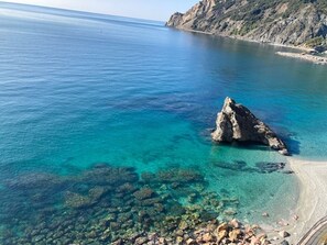 Een kustlandschap met helder turquoise water, een rotsachtige landtong en een zandstrand.