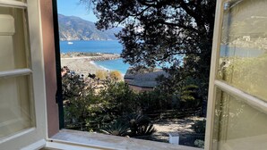 Vista sulla costa attraverso una finestra, con spiaggia, costa rocciosa e una nave all'orizzonte.