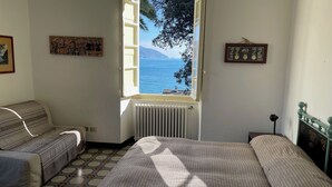 Una camera da letto con un letto, un divano, un termosifone, una finestra vista mare e una parete con un quadro incorniciato.