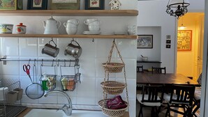 Una cucina con piastrelle bianche, pentole appese e uno scaffale in legno con stoviglie e un'illustrazione incorniciata con pesche.