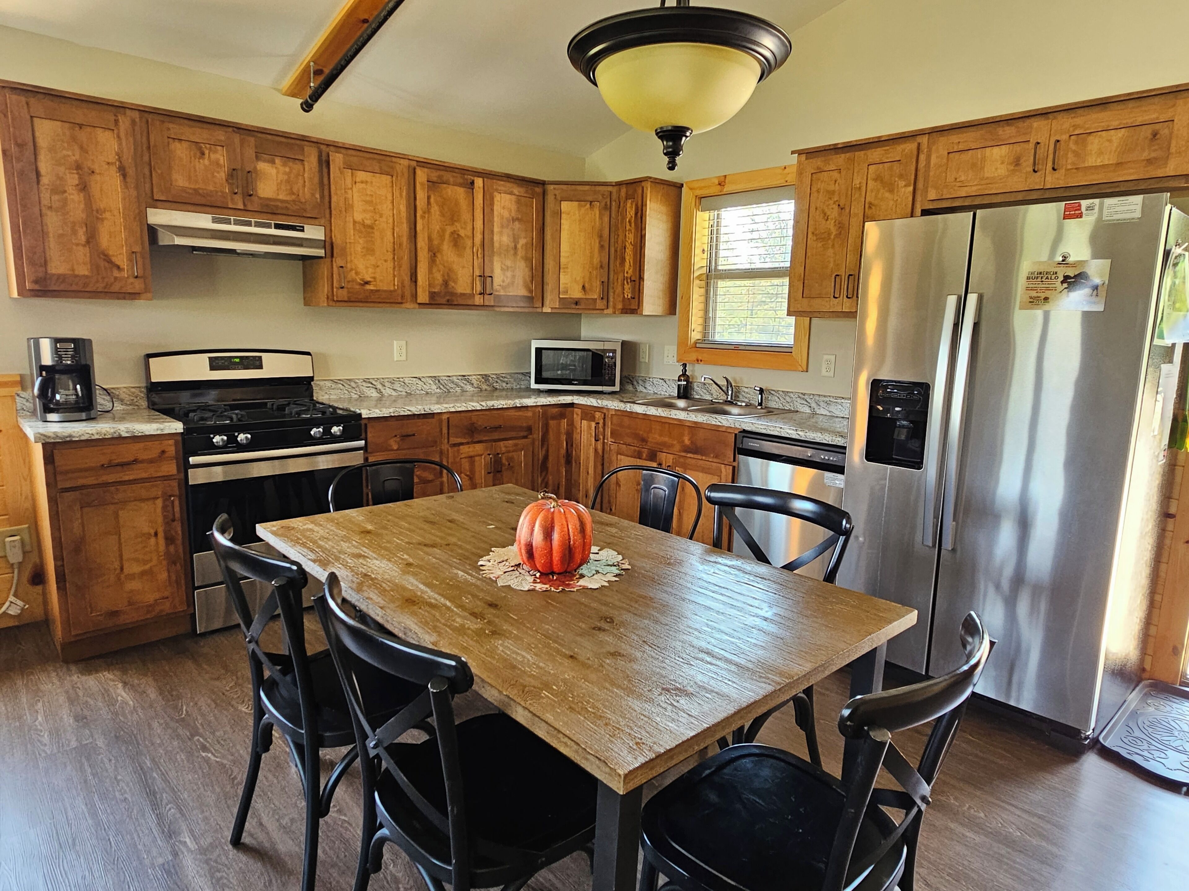 Una cocina con armarios de madera, un refrigerador de acero inoxidable, una estufa y una mesa de comedor con sillas.