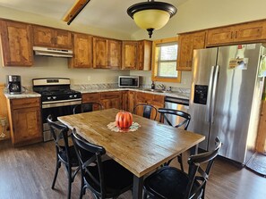A kitchen with wooden cabinets, a stainless steel refrigerator, a stove, and a dining table with chairs.