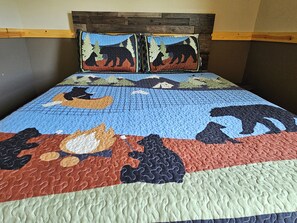 A bed with a quilt featuring animal patterns, a wooden headboard, and a pillow with a similar design.