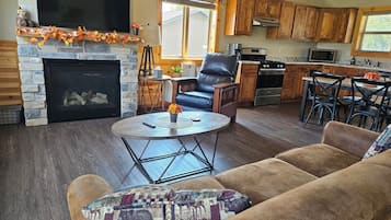 Ein Wohnzimmer mit Kamin, Fernseher und Essbereich, im Hintergrund eine Küche.