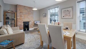 Una sala de estar con chimenea de ladrillo, un sofá, una mesa de comedor con sillas, una estantería y un televisor.