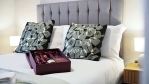 Una cama bien hecha con almohadas estampadas, una caja de artículos de aseo y una mesita de noche con lámpara.