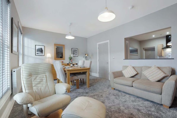 A living room with a sofa, armchair, dining table, and chairs.
