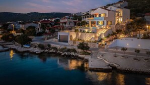 Ein modernes Küstenhaus mit Pool, umgeben von anderen Gebäuden und Hügeln.