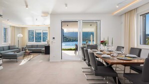 Ein modernes Wohnzimmer mit Sofa und Couchtisch, ein Essbereich mit Tisch für vier Personen und eine große Schiebeglasdoor zum Balkon mit schöner Aussicht.