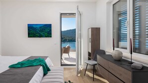 Ein modernes Schlafzimmer mit Bett, Stuhl, Kommode und großem Fenster mit Blick auf einen See und Hügel.
