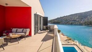 Ein Balkon mit roter Wand, einem Pool und Blick auf einen See und Hügel.