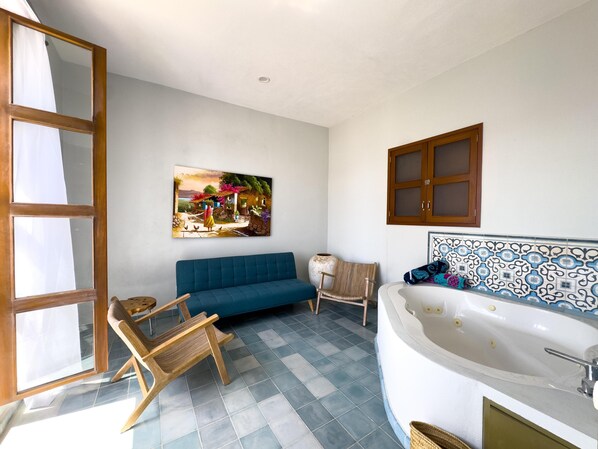 Een badkamer met een blauwe bank, houten stoelen, een groot bad en een schilderij aan de muur.
