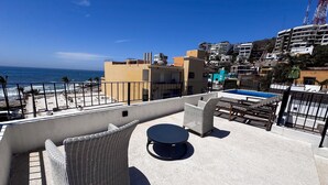 A rooftop terrace with wicker furniture, a pool, and a view of the ocean and buildings. - Centro Historico on the Malecon Boardwalk (Mazatlan)