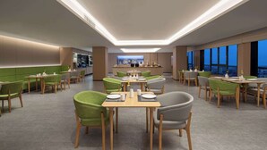 Un comedor moderno con sillas verdes y grises, mesas de madera y una zona de bar central.